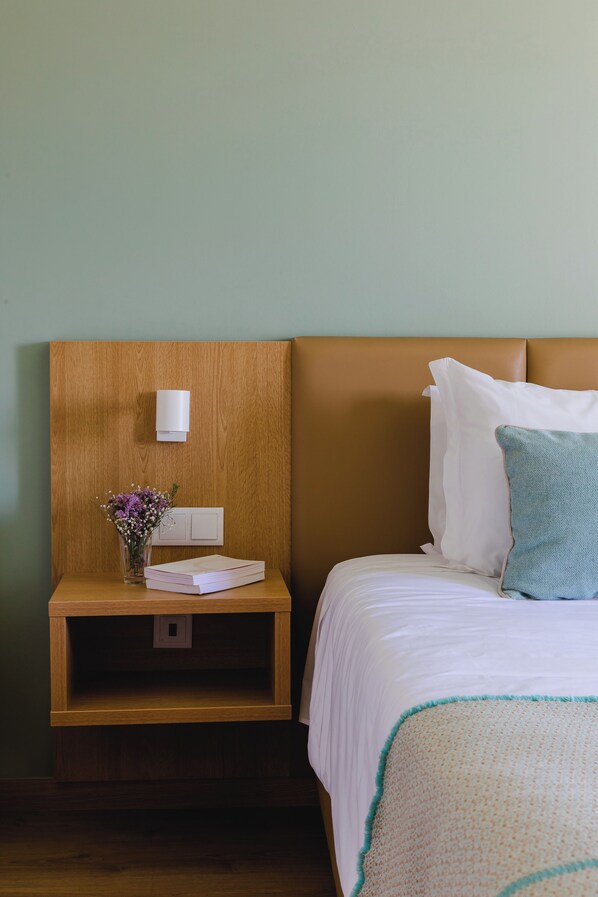 A neatly made bed with white bedding and a teal throw, a wooden nightstand with a vase of flowers, and a wall-mounted light. - Santo Antonio de Fatima (Ourem)