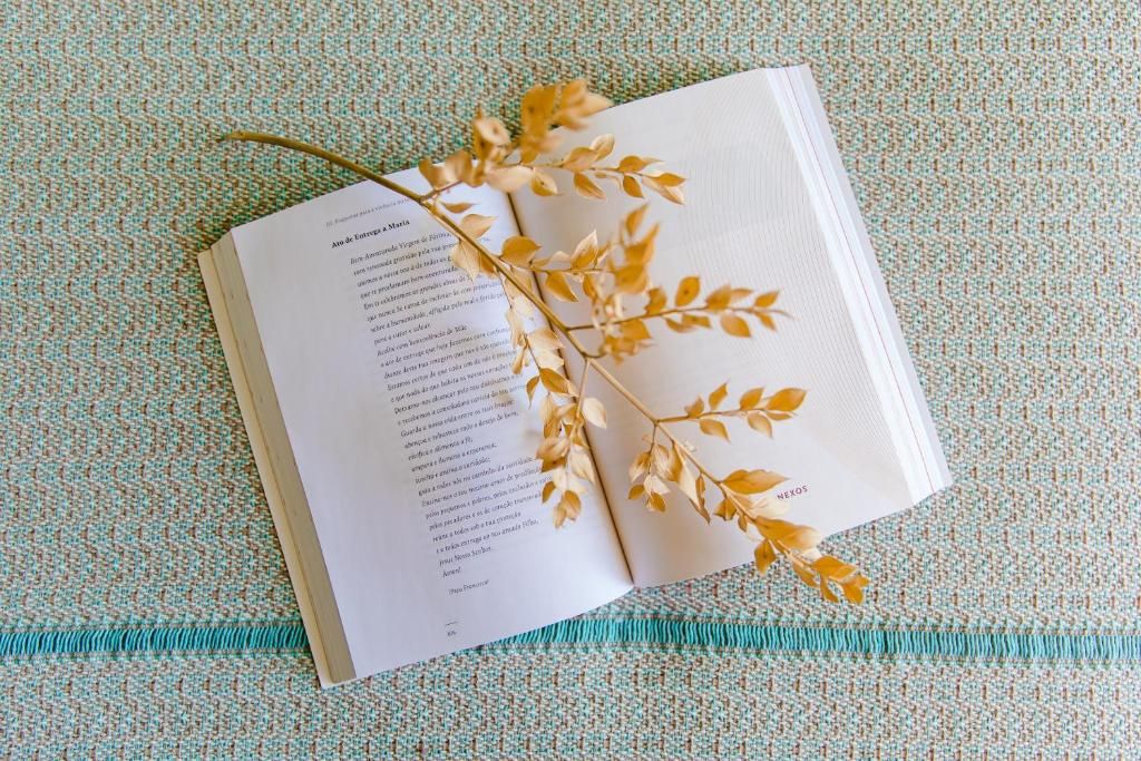 Un libro abierto con una rama encima, sobre una superficie de tela texturizada.