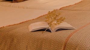 Een netjes opgemaakt bed met een bruin kussen, een wit kussen, en een boek met een gedroogde bloem erop.