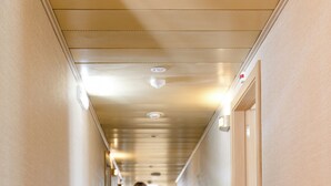 Een hotelgang met vloerbedekking, deuren aan weerszijden en een persoon die met een koffer loopt.