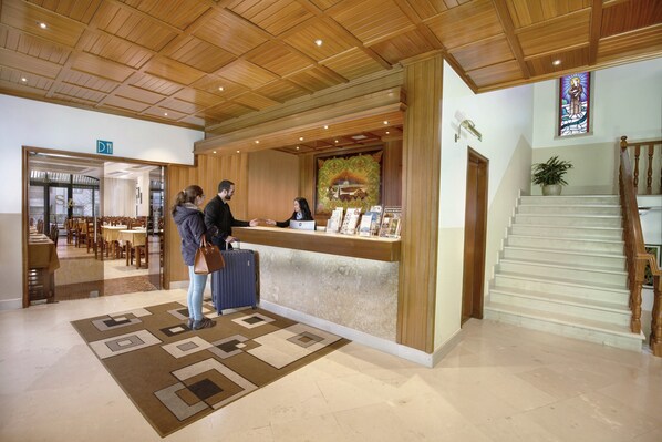 Un área de recepción con un mostrador de madera, una escalera y una alfombra estampada.