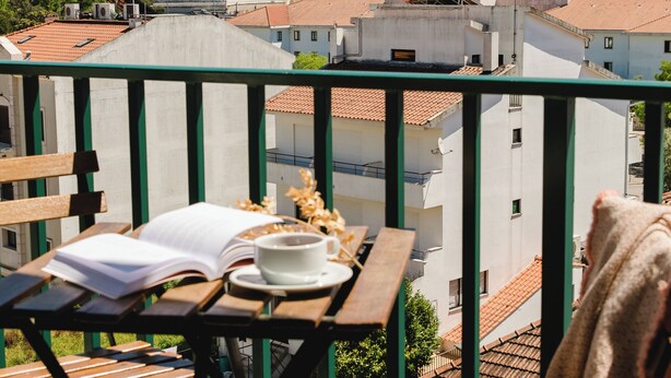 Een balkon met uitzicht op een historisch gebouw, een tafel met een boek en een kopje, en een stoel.