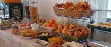 A buffet with various food items including fruits, pastries, and bread.