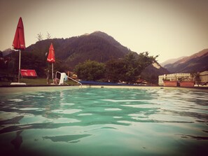 Una piscina con agua cristalina, rodeada de montañas y árboles.