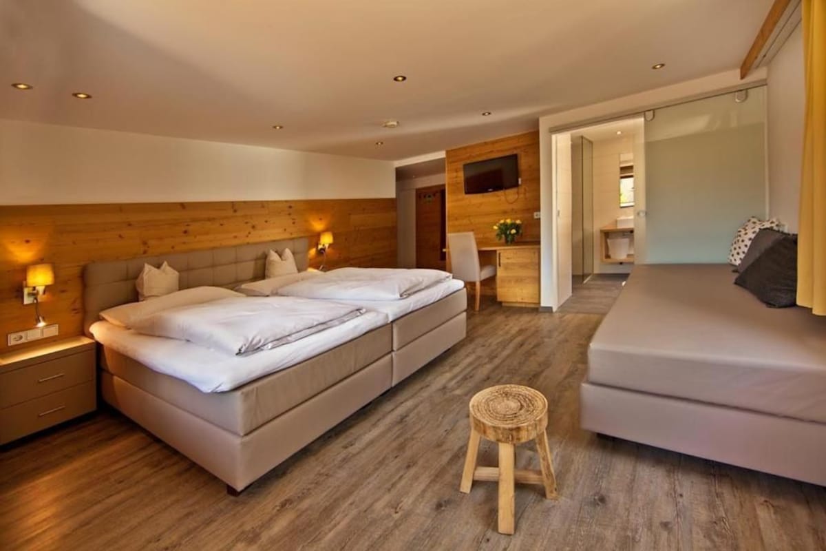 A modern hotel room with a large bed, a smaller bed, a seating area, and a television.