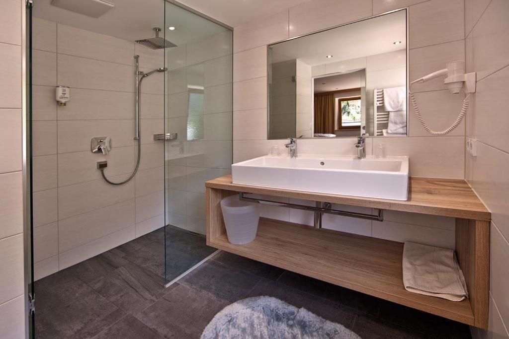 A modern bathroom with a glass-enclosed shower, a large mirror, and a wooden vanity.