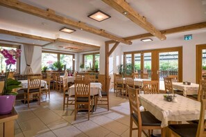 Un restaurant avec des poutres en bois, un sol carrelé et des tables recouvertes de nappes blanches.