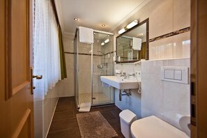 Un baño moderno con cabina de ducha de vidrio, un lavabo blanco y un inodoro.