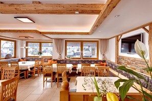 Un restaurant avec des poutres en bois, de grandes fenêtres et un agencement varié des sièges, comprenant des tables et des bancs.