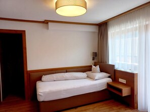 Habitación de hotel con cama, mesita de noche, lámpara y ventana con cortinas.