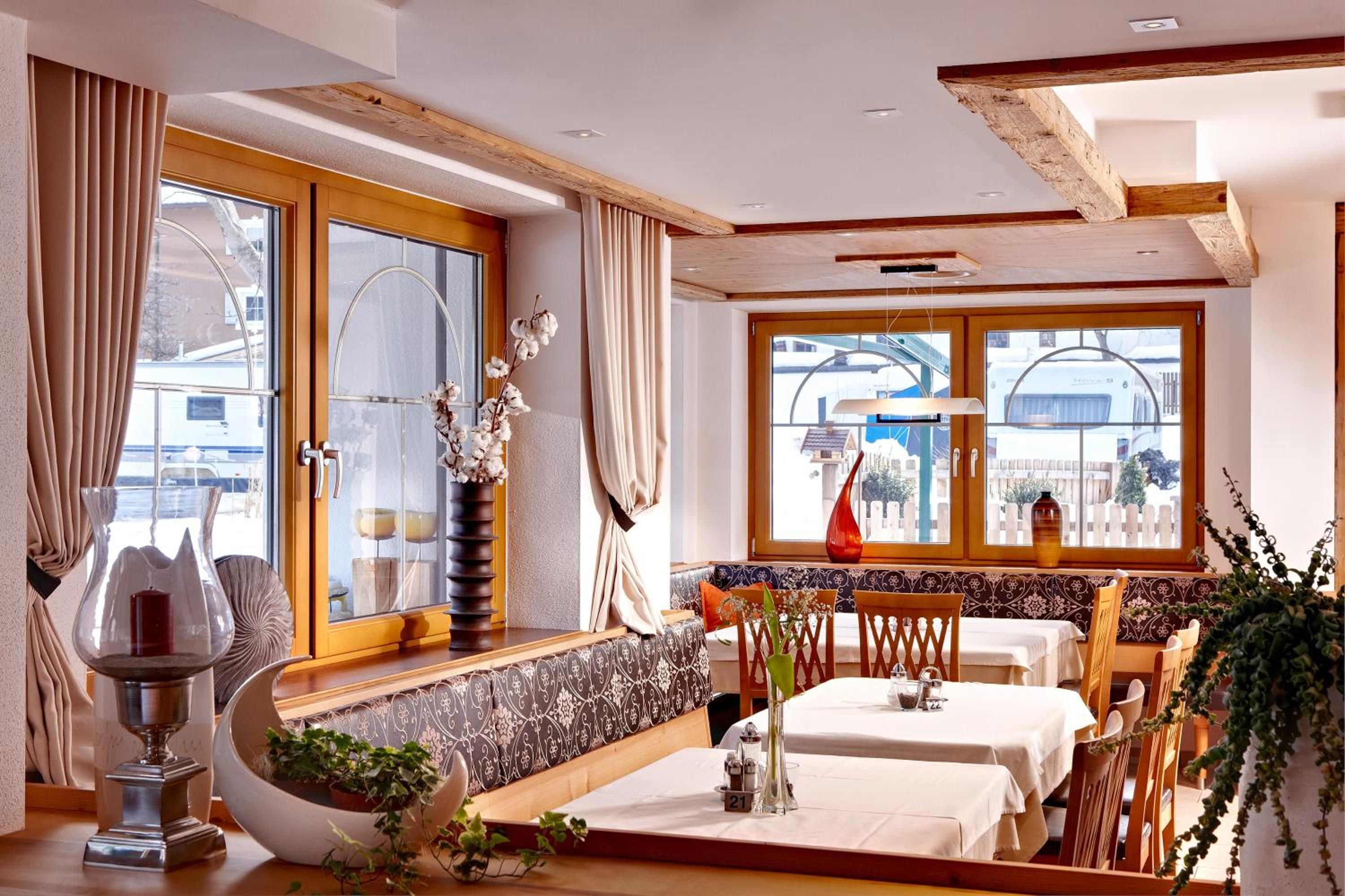 A dining area with a high wooden ceiling, large windows, and a view of the outside. There are two tables set for dining, a bench, and a decorative vase with flowers.