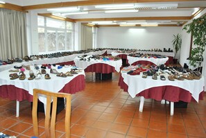 A room with multiple tables covered with white cloths and red borders, displaying various shoes. - Estalagem Cruz Da Mata (Mangualde)