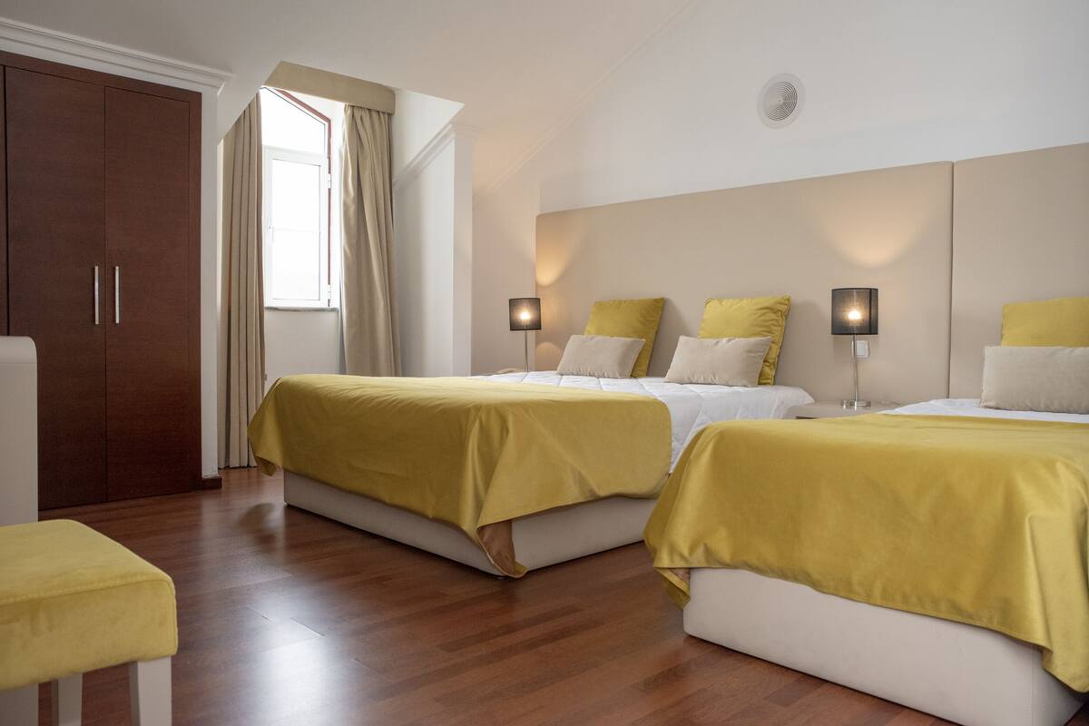 Ein Hotelzimmer mit zwei Betten, einem Kleiderschrank, einem Fenster mit Vorhängen und Nachttischlampen.