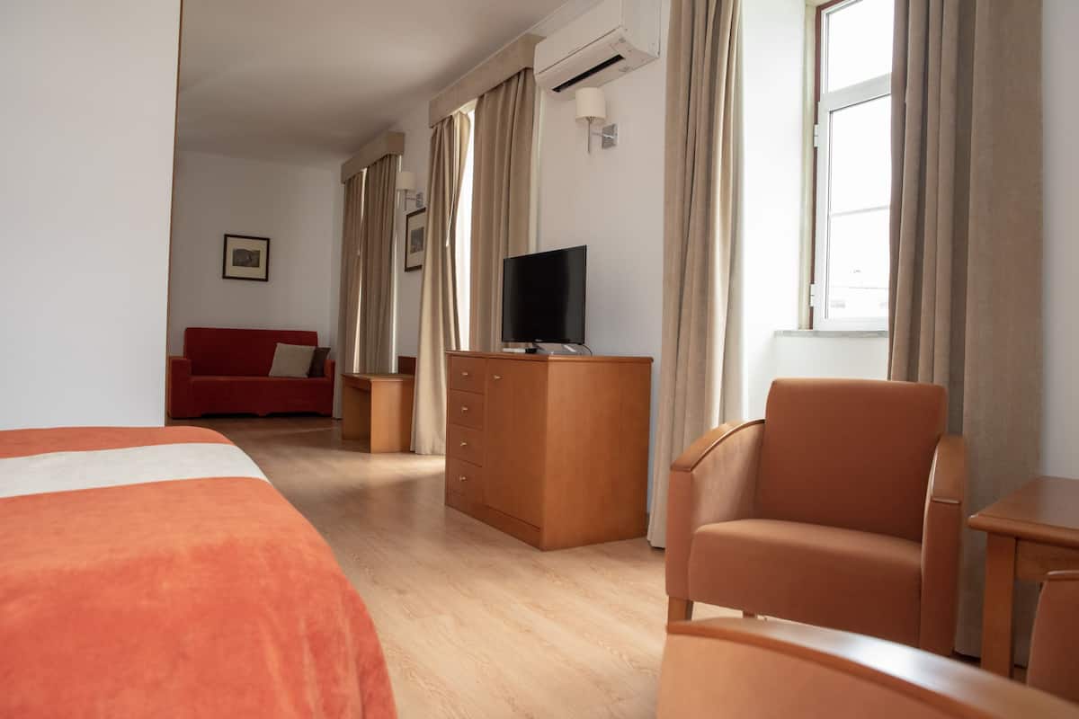 Ein Hotelzimmer mit Bett, Schreibtisch, Fernseher, Stuhl und einem roten Sofa.