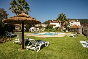 Uma área de piscina com espreguiçadeiras e um guarda-sol de palha.