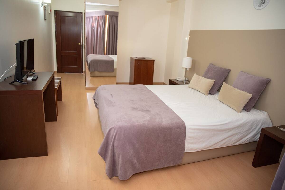 Ein Hotelzimmer mit Bett, Nachttisch, Lampe und Schreibtisch mit Computer und Telefon.