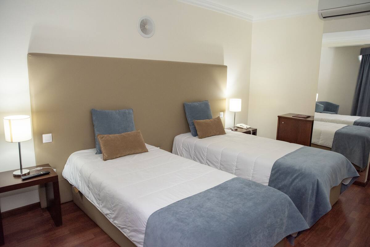 Ein Hotelzimmer mit zwei Betten, einem Nachttisch, einer Lampe und einem Spiegel.