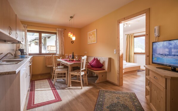 Una cocina acogedora con comedor, muebles de madera, un televisor y una ventana con cortinas.