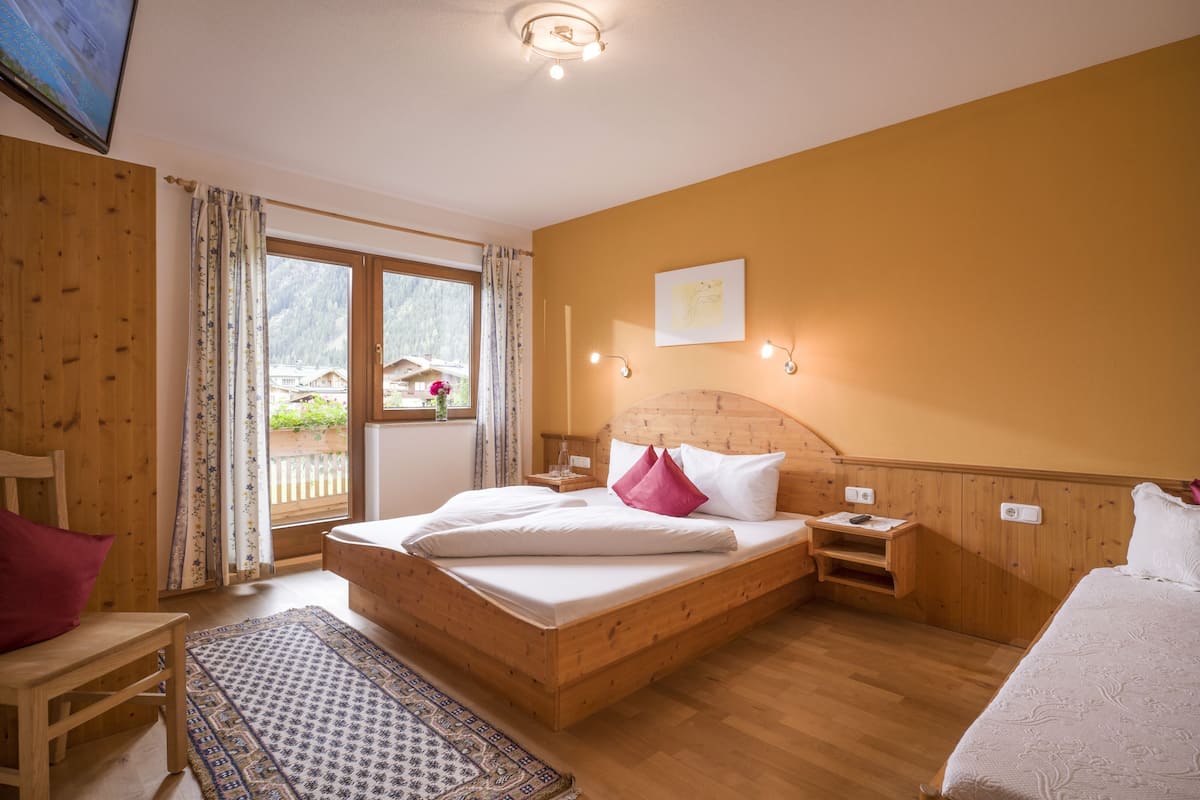 A wooden-framed bedroom with a bed, a nightstand, a chair, and a window with curtains.