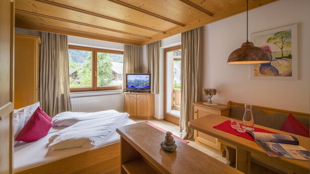 A room with a bed, a wooden table, a television, and a window with curtains. - Landhaus Gasser (Mayrhofen)