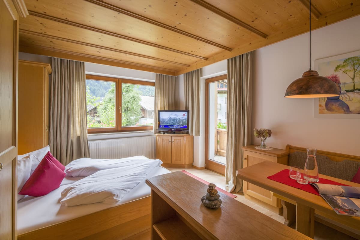 A room with a bed, a wooden table, a television, and a window with curtains.