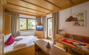 Una habitación con cama, una mesa de madera, televisión y ventana con cortinas.
