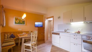 A compact kitchen with white cabinets, a built-in oven, and a dining area with a wooden table and chairs. - Landhaus Gasser (Mayrhofen)