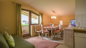 A cozy living room with a green sofa, a dining area with wooden furniture, a kitchen with a refrigerator, and a TV on the counter. - Landhaus Gasser (Mayrhofen)