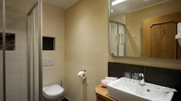 Un baño moderno con cabina de ducha de vidrio, inodoro, lavamanos con espejo y una ventana pequeña.