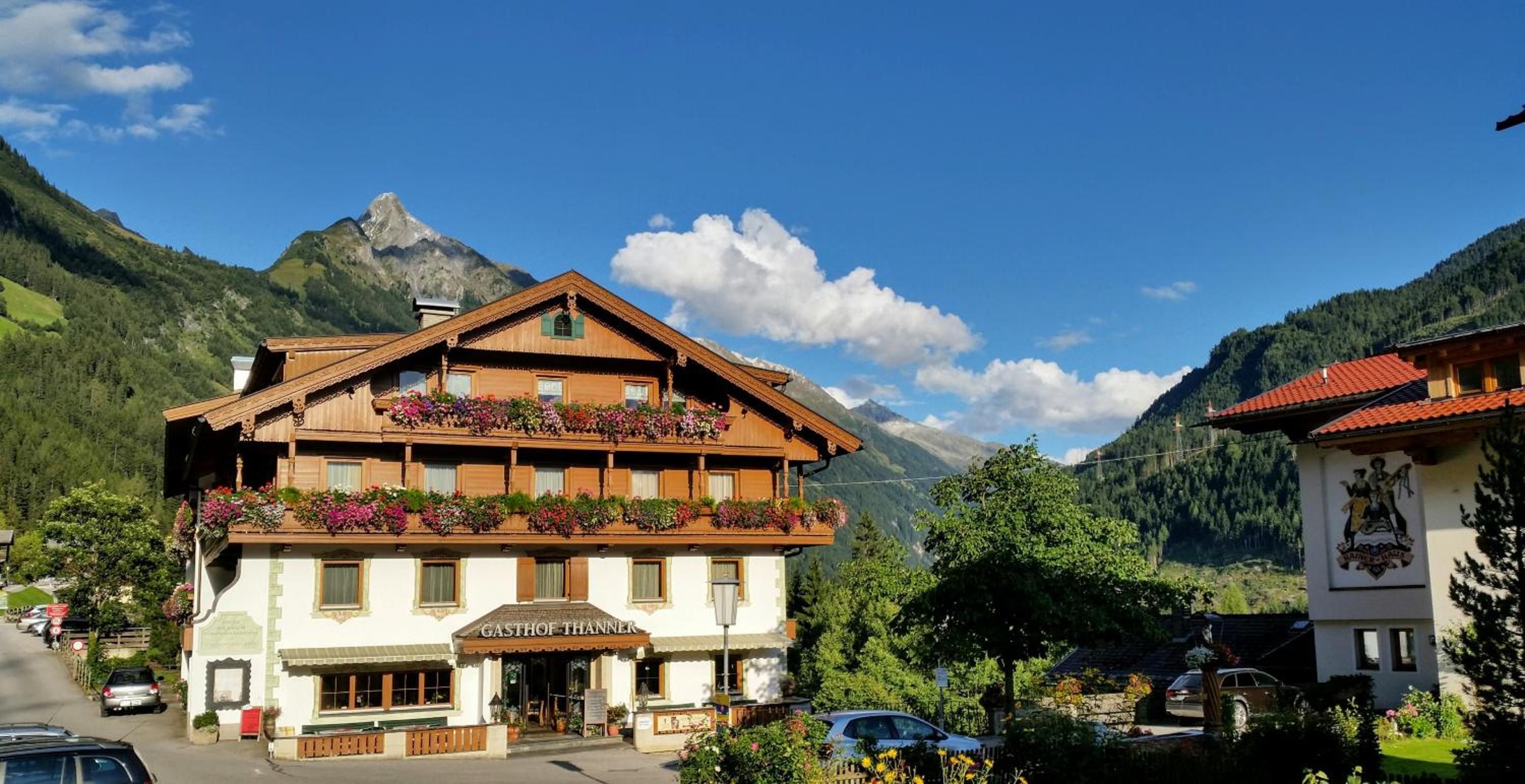 A traditional wooden building with a sign reading 'GASTHOF THANNER' in a mountainous area with a clear sky.