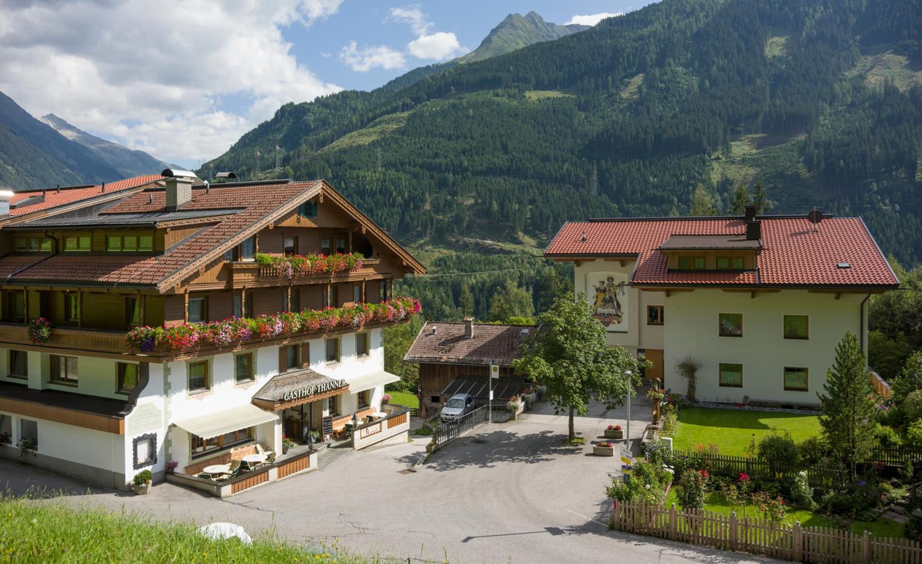 A traditional Alpine-style building with a balcony, a sign reading 'GASTHOF THANNER,' and a mountainous backdrop.