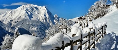 A snow-covered mountain landscape with a wooden fence and a cabin in the background.