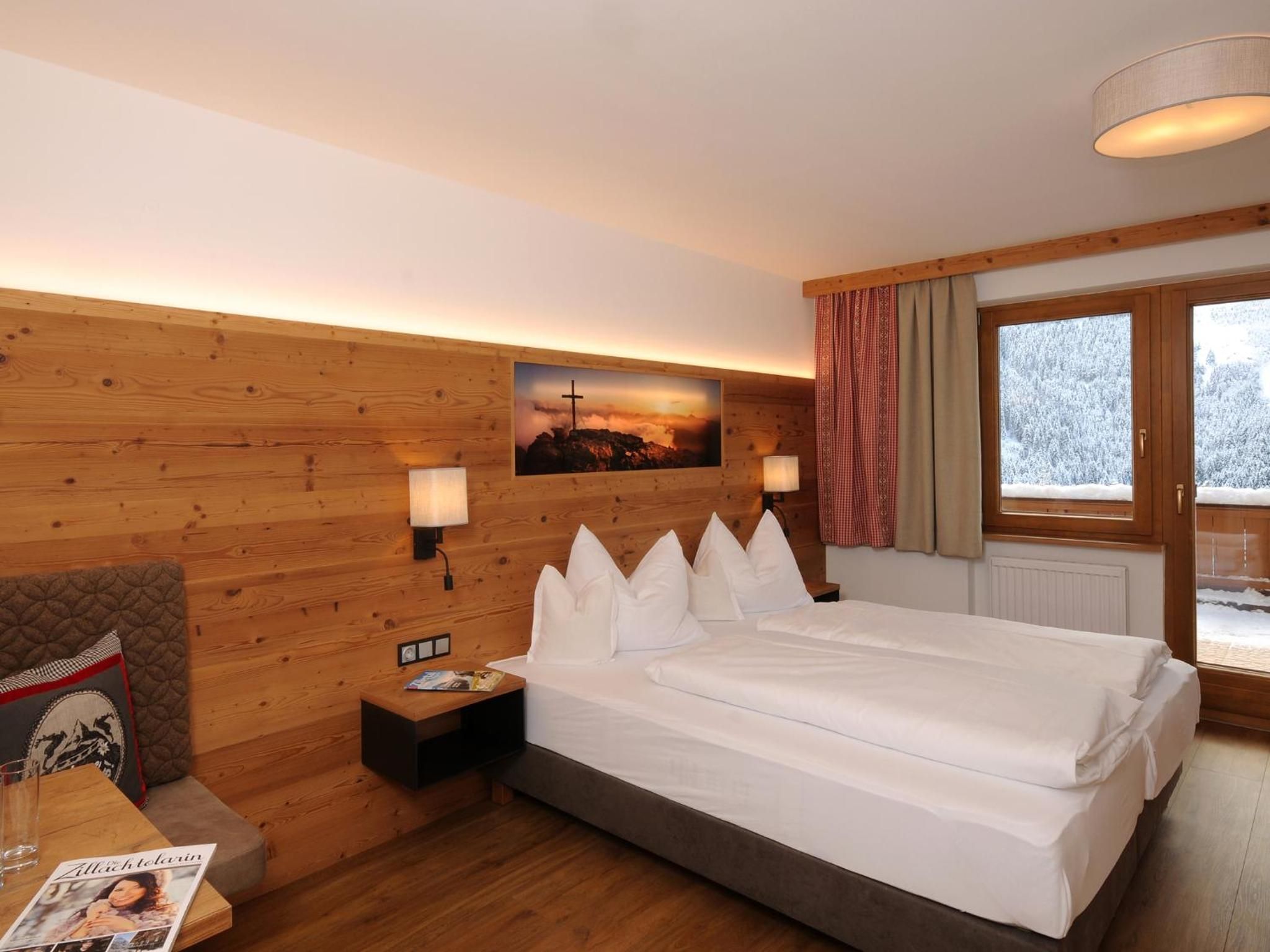 Habitación de hotel con pared de madera, cama con ropa blanca, mesita de noche, lámpara, ventana con cortinas y un cartel en la pared.