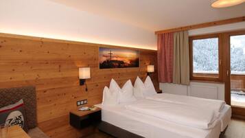 Habitación de hotel con pared de madera, cama con ropa blanca, mesita de noche, lámpara, ventana con cortinas y un cartel en la pared.