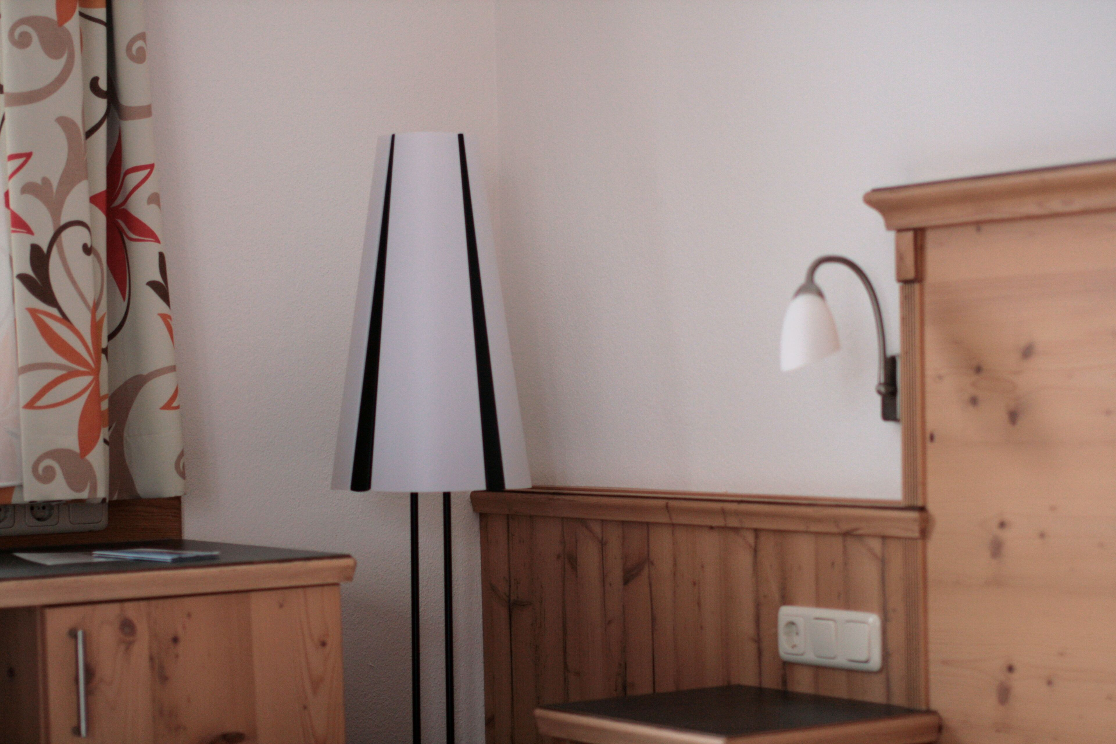 A corner of a room with a wooden cabinet, a lamp, and a wall-mounted light fixture.