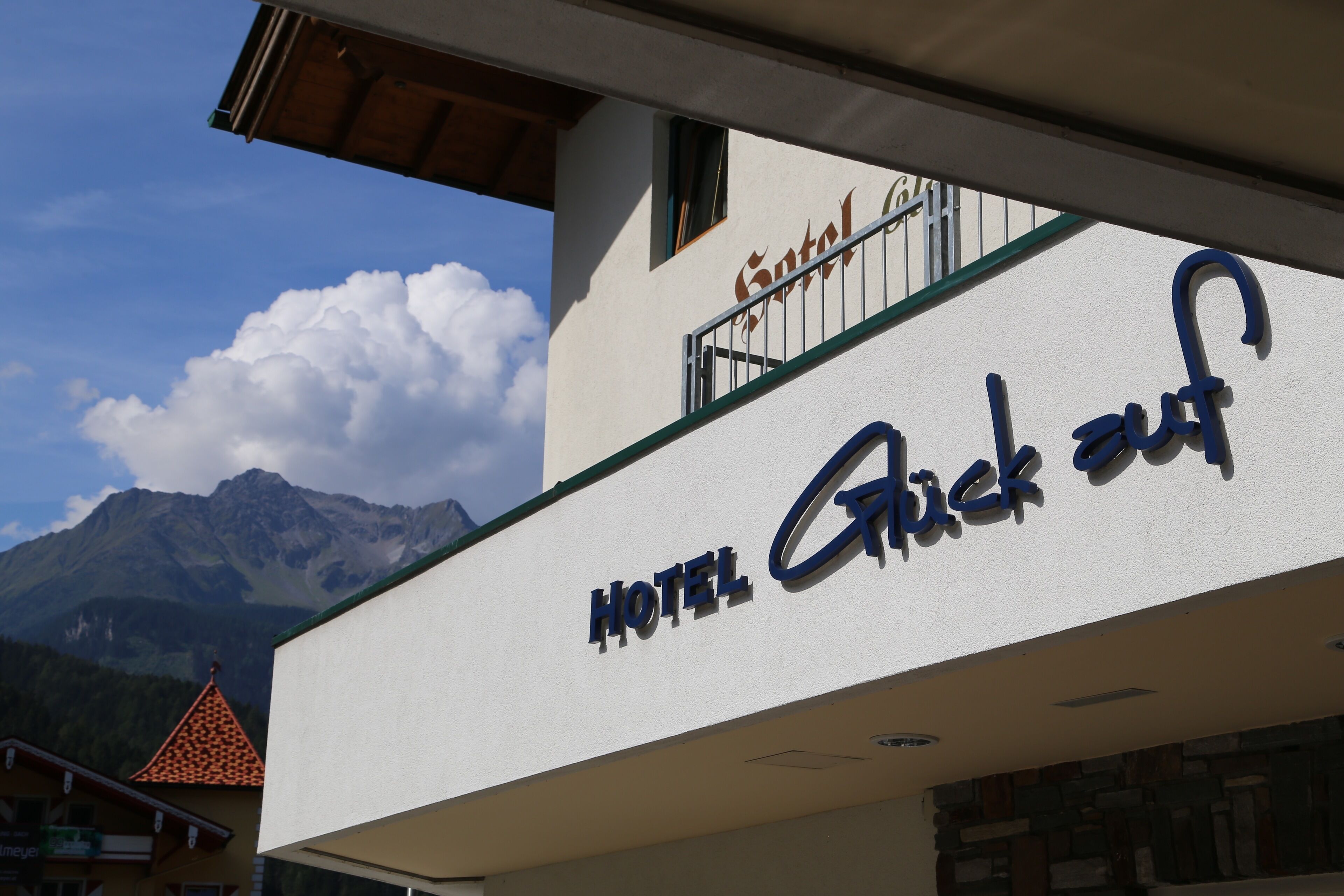 Et hotelskilt med navnet "HOTEL Greck auf" og et bjerg i baggrunden.