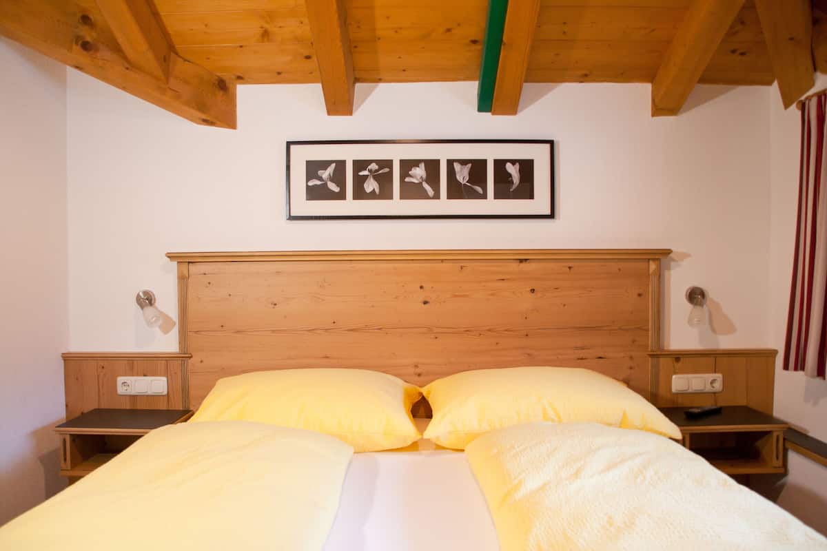 A bedroom with a wooden headboard, a bed with yellow bedding, two bedside tables, and a framed picture of flowers on the wall.