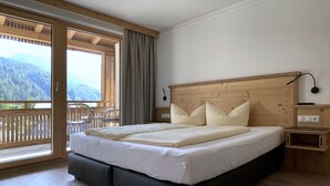 A bedroom with a wooden headboard, a large bed with white bedding, a bedside table, and a view of mountains through a sliding glass door. - Glück auf (Mayrhofen)