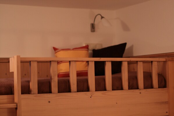 A wooden bunk bed with a headboard, a wall-mounted light fixture, and a cushion with a red and yellow design. - Glück auf (Mayrhofen)