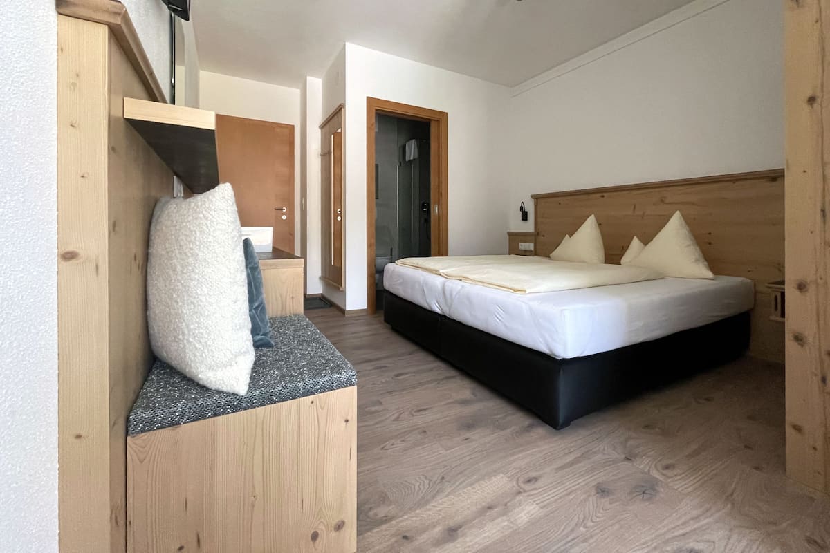 A bedroom with a wooden headboard, a bed with white bedding, a small bedside table, and a wooden bench with a cushion.