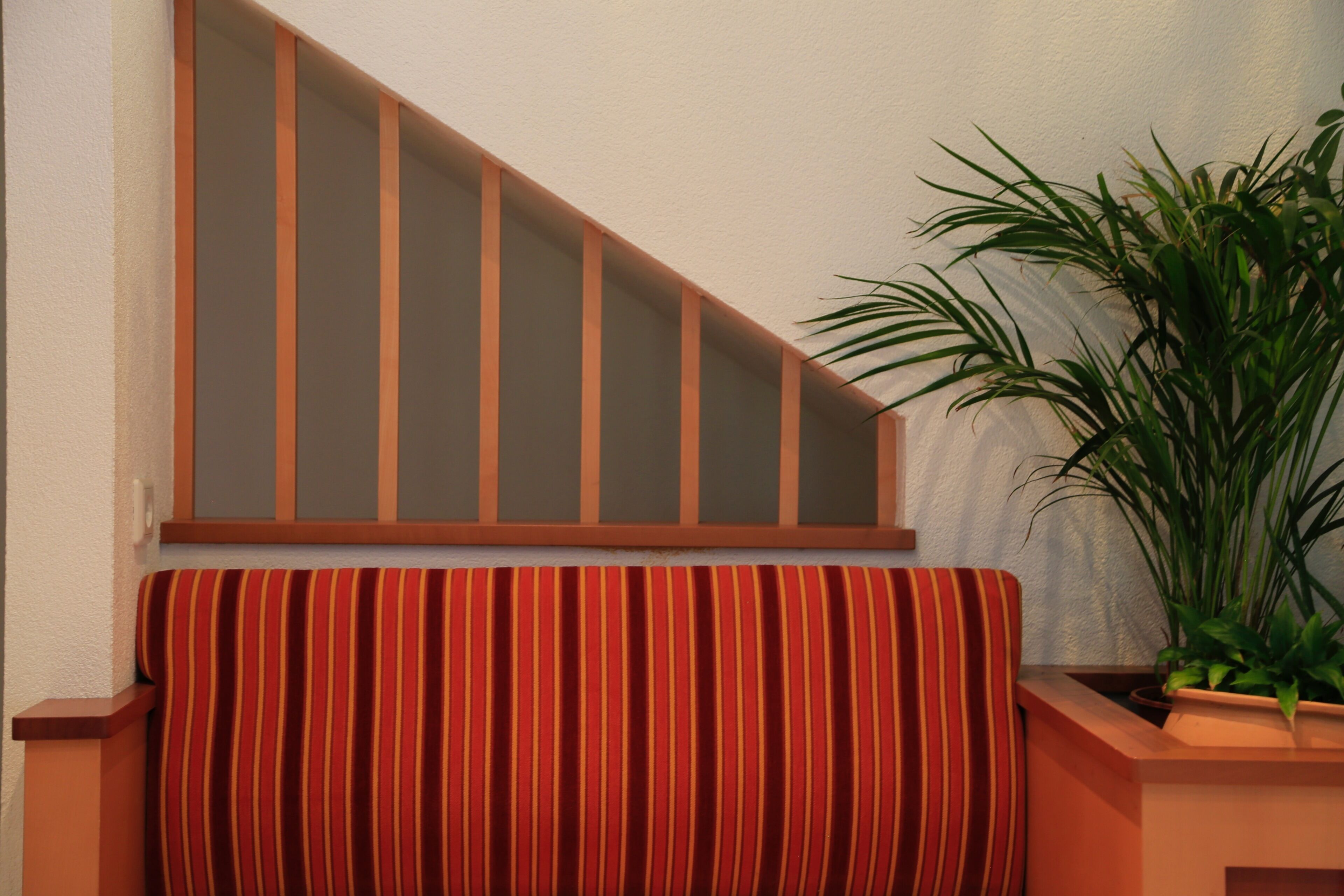 Una escalera con barandillas de madera y un cojín a rayas rojo y amarillo al pie.