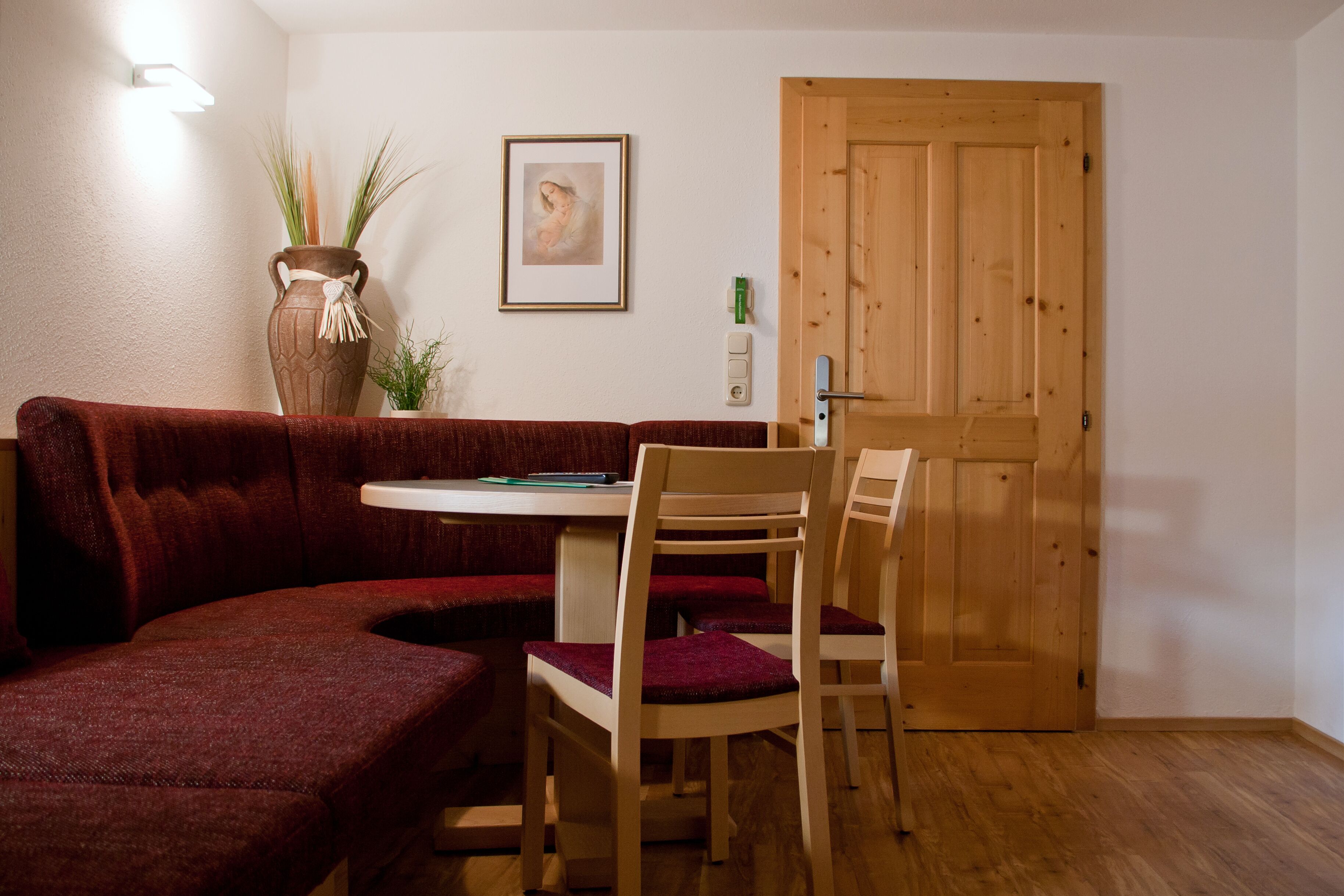 A cozy room with a wooden door, a red sofa, a small table, and a chair.