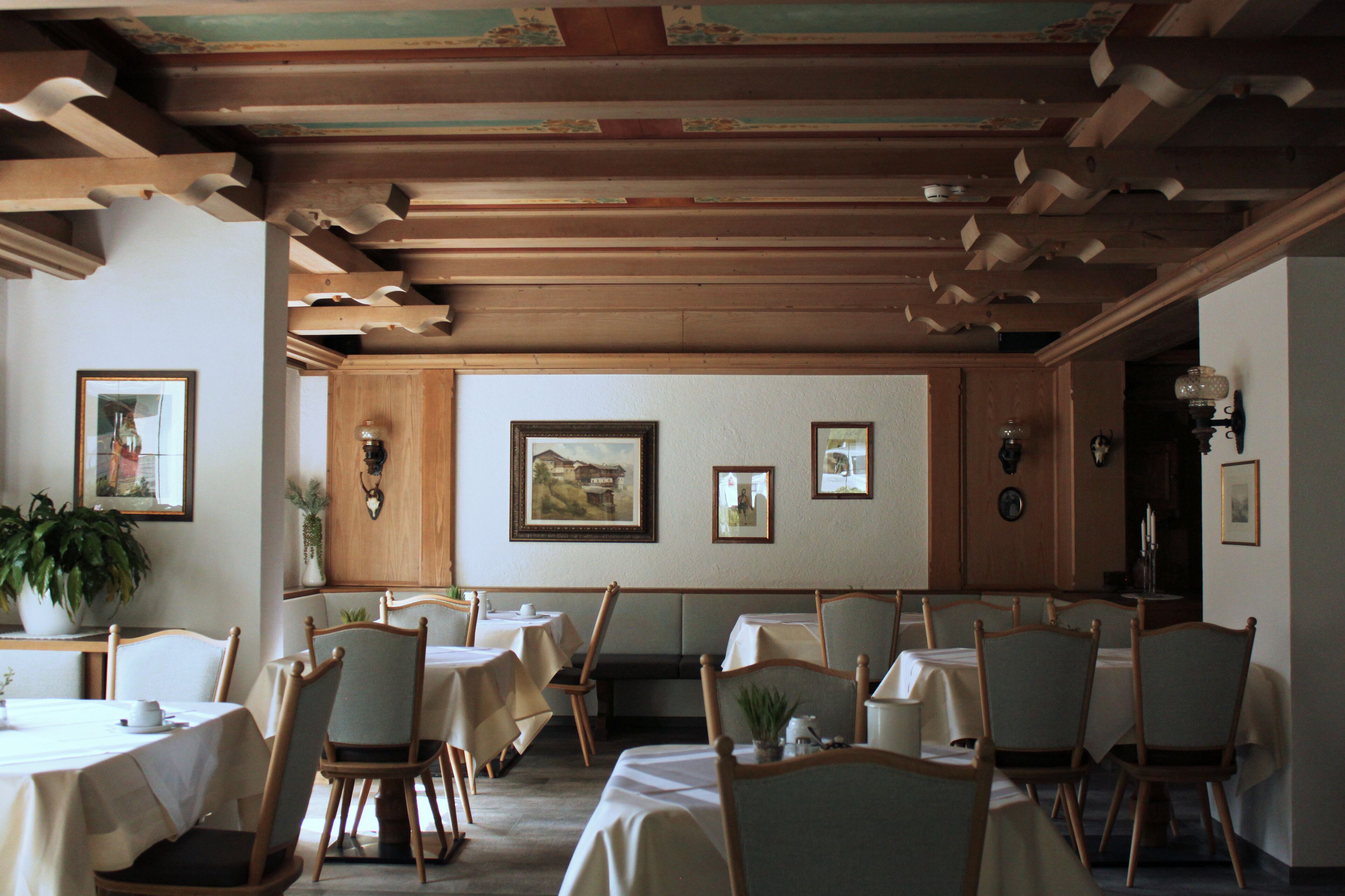 A dining area with wooden beams, tables, chairs, and framed artwork on the walls.