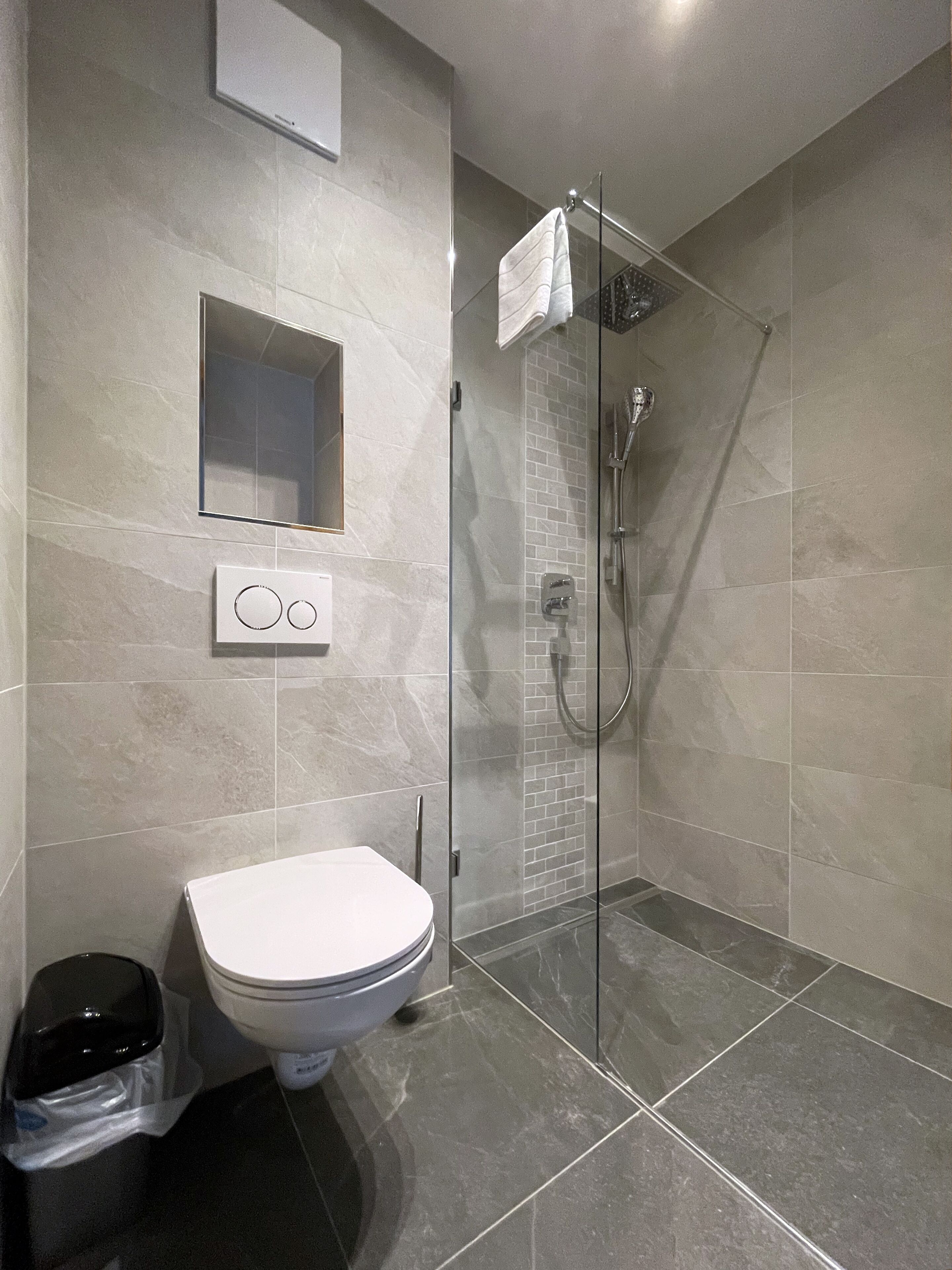 Un baño moderno con ducha envuelta en vidrio, inodoro y panel de control en la pared.