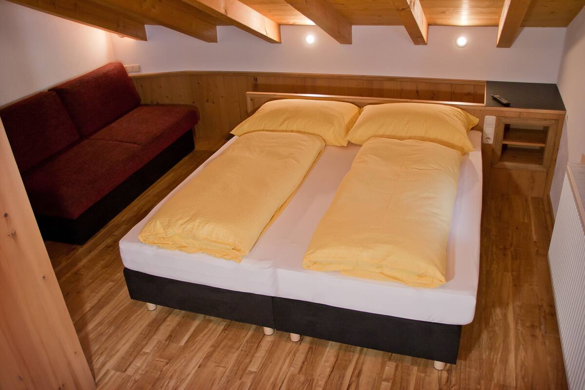 A room with a bed, a red sofa, and a wooden ceiling.