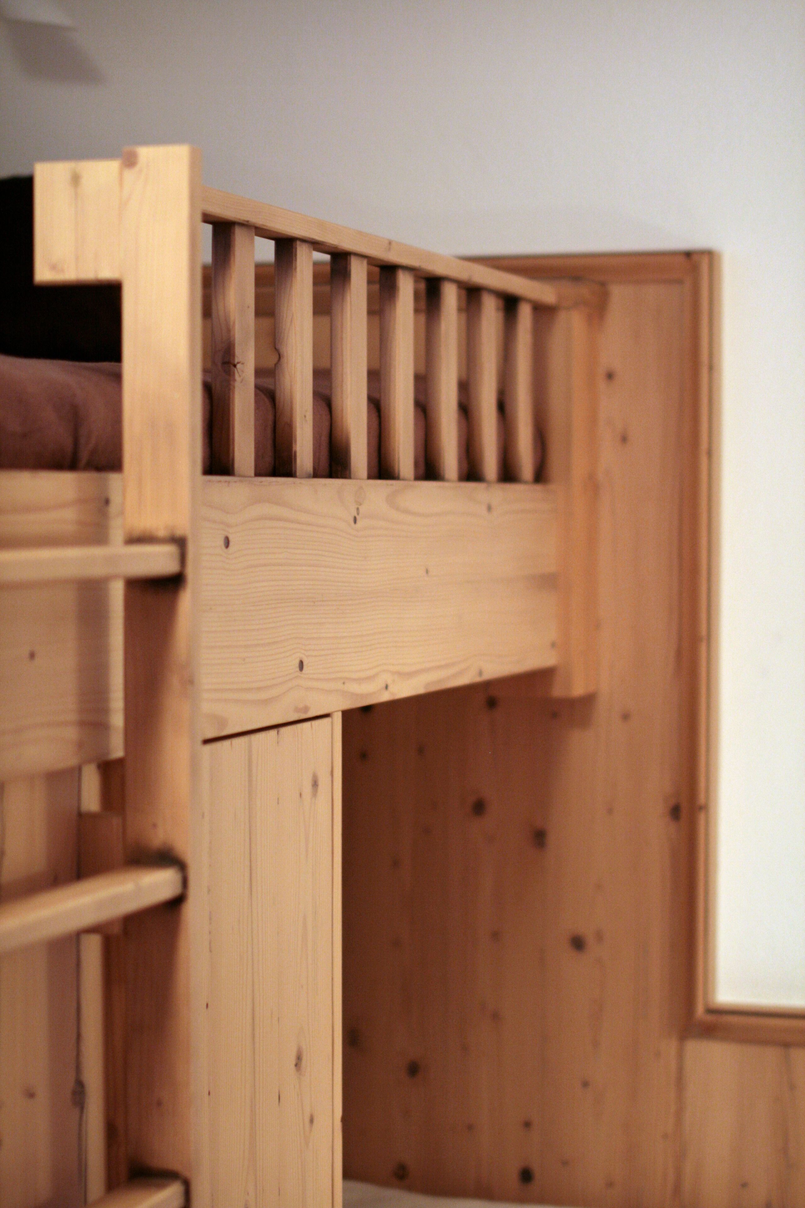 A wooden bunk bed with a ladder, a lower shelf, and a headboard.