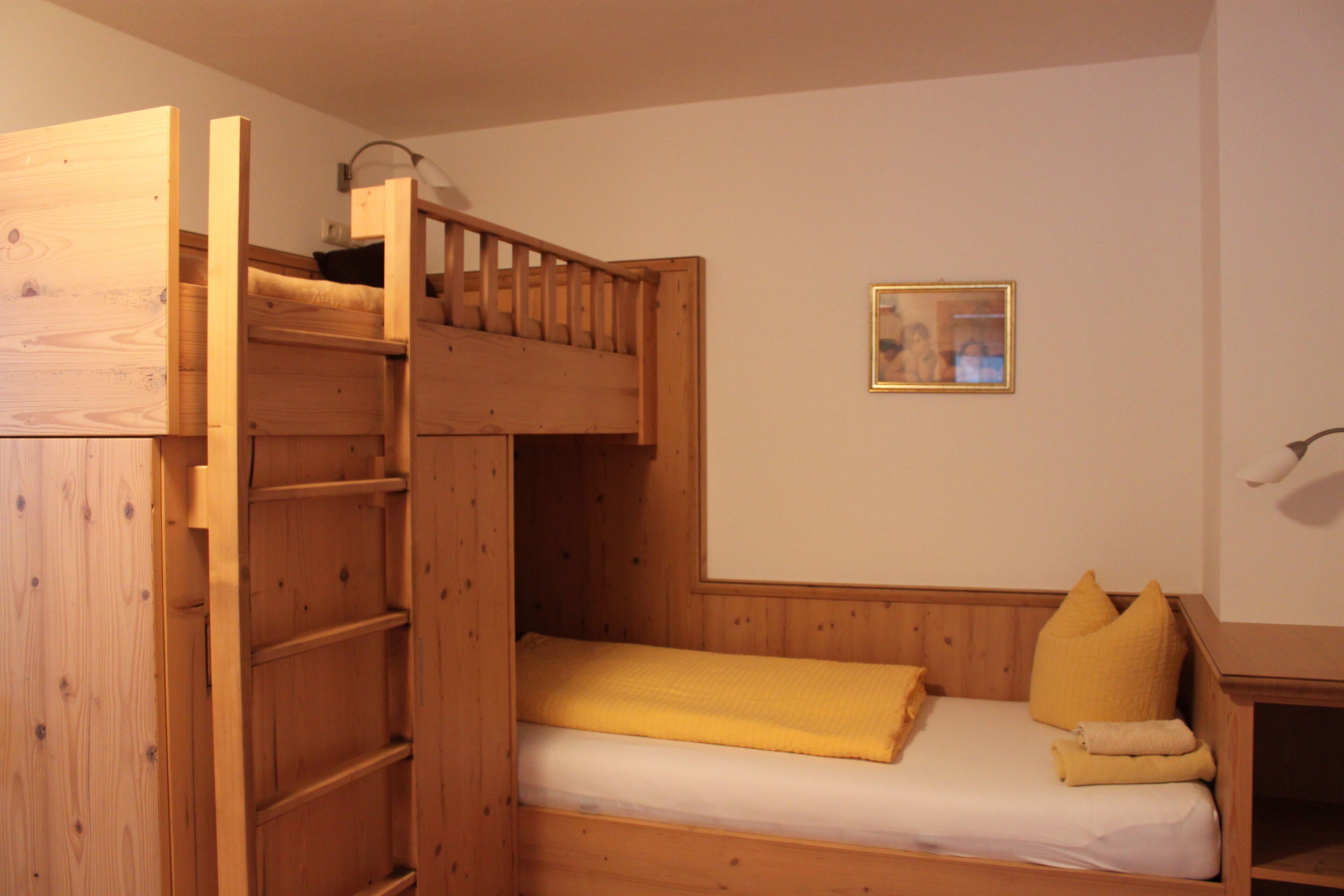 A bunk bed room with a wooden ladder, a small table, and a framed picture on the wall.