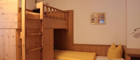 A bunk bed room with a wooden ladder, a small table, and a framed picture on the wall.