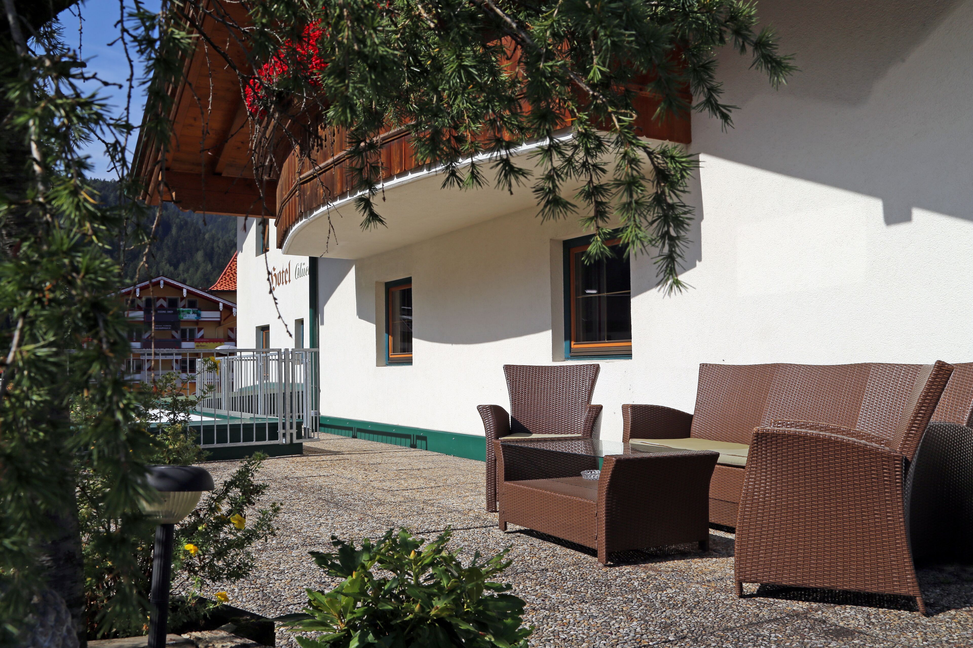 An outdoor seating area with wicker furniture, a white building with a green trim, and a wooden pergola with red flowers.