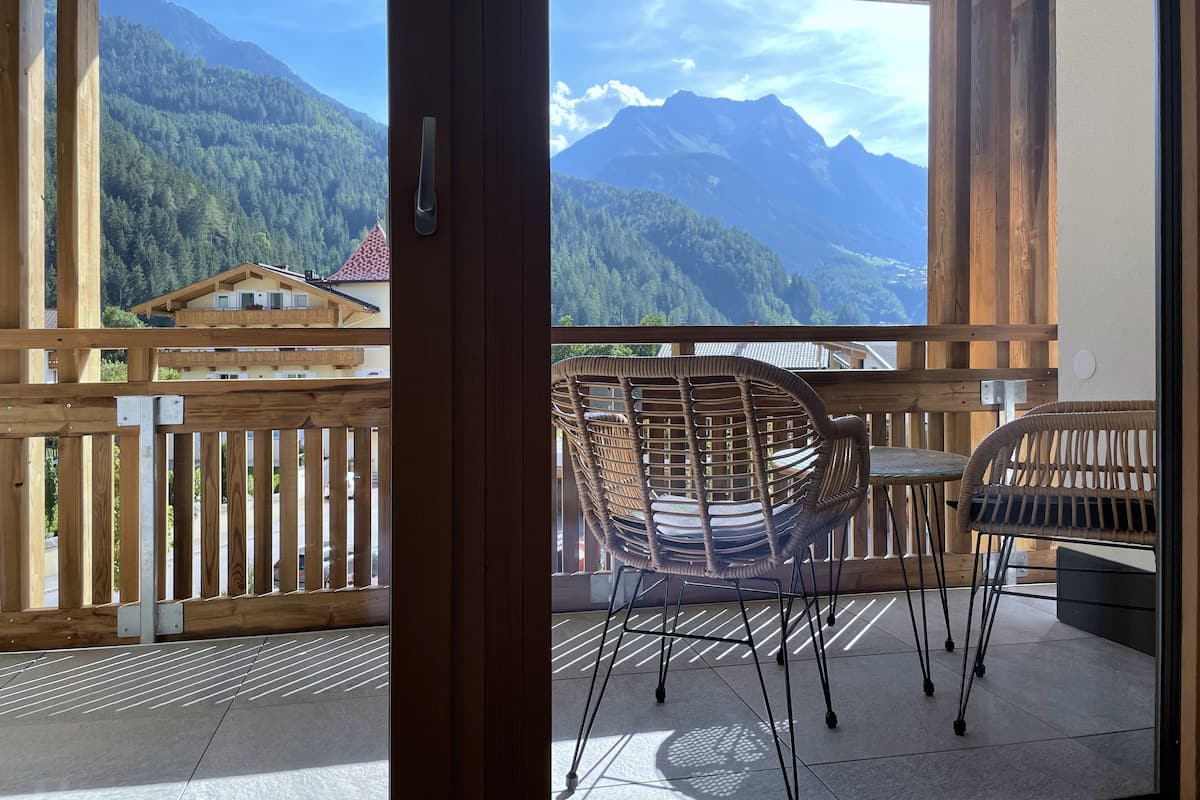 A wooden balcony with wicker chairs and a table, overlooking a mountainous landscape.